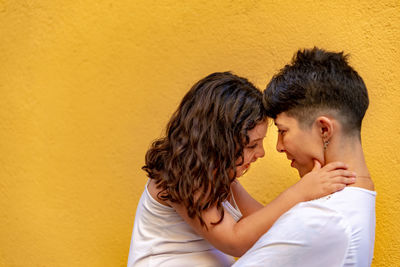 Side view of couple kissing against orange wall