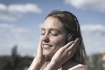 Close-up of young woman listening to music against sky