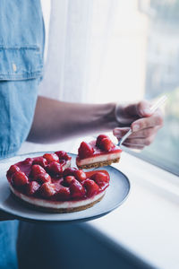 Midsection of woman having sweet food by window