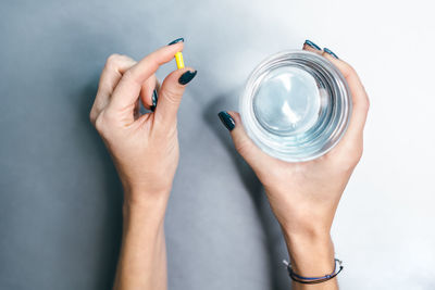 Hands of caucasian girl with yellow pill in left palm and glass of water in right hand. 