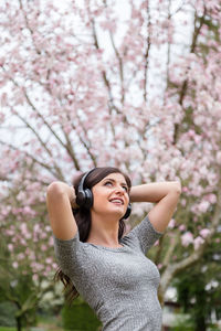 Low angle view of young woman standing against pink cherry blossom