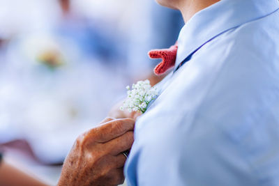 Close-up of woman putting flower on shirt of bridegroom