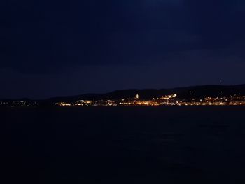 Illuminated city by sea against sky at night