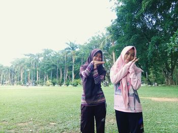 Happy friends sitting on grass against trees