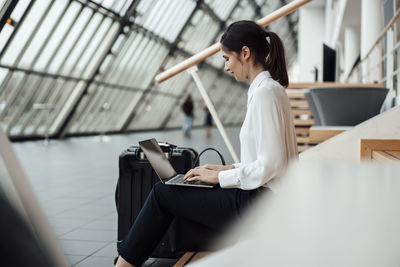 Businesswoman working on laptop while sitting in office corridor