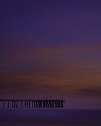 Silhouette wooden post on pier over sea against sky during sunset