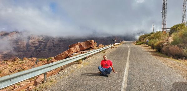 Rear view of man sitting on road against sky