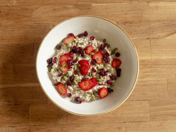 A bowl of oatmeal with strawberries on a wooden table. view from above.