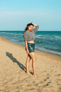 Portrait of young woman standing at beach against sky