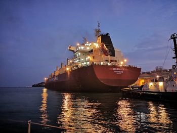 Illuminated commercial dock by sea against sky at night