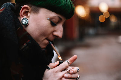Portrait of non-binary hipster woman lighting a cigarette in city