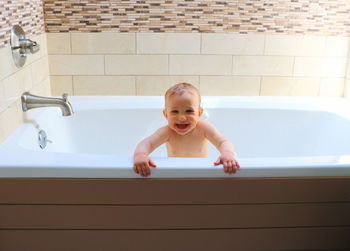 High angle view of cute smiling baby taking a bath, standing in a bathtub