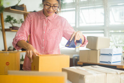 Young woman sticking adhesive tape on cardboard box at home