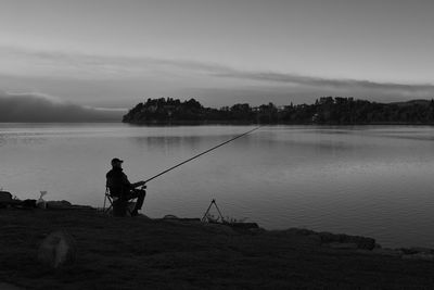 Scenic view in black and white of lake against sky with fisherman