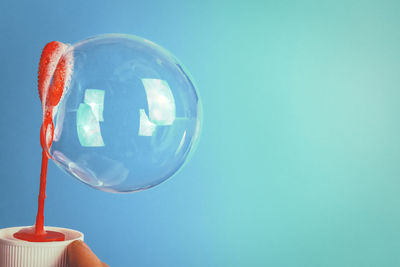 Close-up of hand holding bubble against blue background