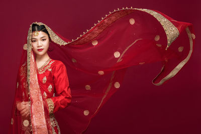 Portrait of beautiful young bride standing against red background