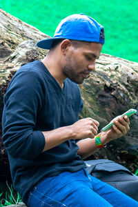 Side view of young man sitting with his phone on the rock