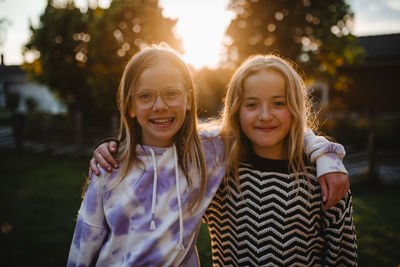 Portrait of happy female friends with arms around at sunset