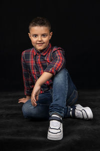 Portrait of boy sitting against black background