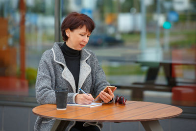 Young woman using mobile phone while sitting on table