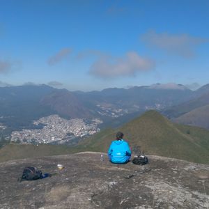 Man sitting on mountain against blue sky