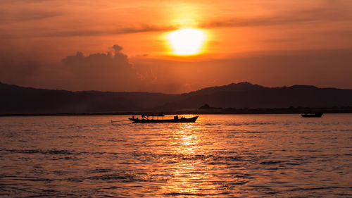 Silhouette boat in sea against orange sky