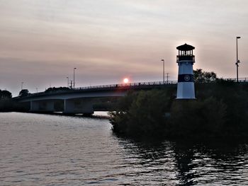 Lighthouse by river against sky during sunset