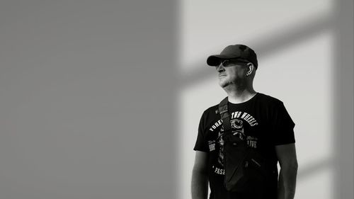 Young man looking away while standing against wall