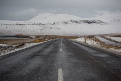 Road leading towards snowcapped mountains against sky