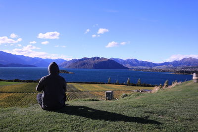 Rear view of man sitting on land against sky