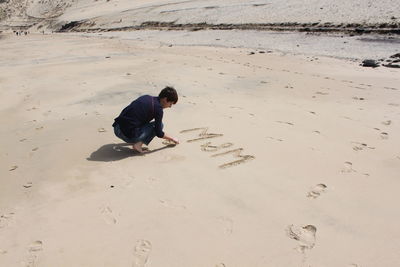 View of woman writing in sand on the beach