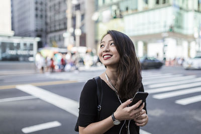 Usa, new york city, manhattan, young woman listening music with cell phone and earphones on the street