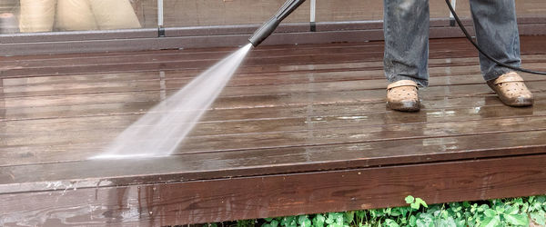 Man cleaning walls and floor with high pressure power washer. washing terrace wood planks and claddi