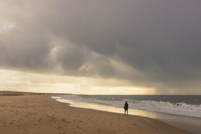 Silhouette man standing at beach against cloudy sky