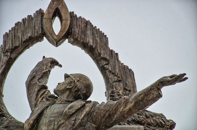 Low angle view of bird perching on statue against sky