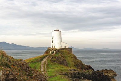 Lighthouse amidst sea and buildings against sky