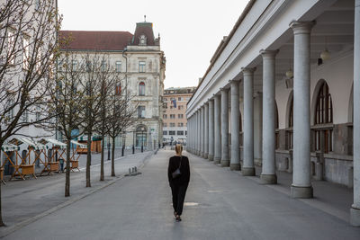 Rear view of man walking on street amidst buildings in city