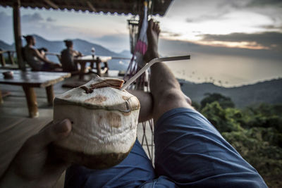 Low section of man holding coconut against sky