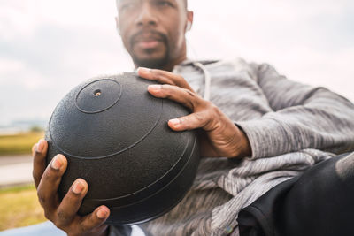 Midsection of man holding ball sitting outdoors