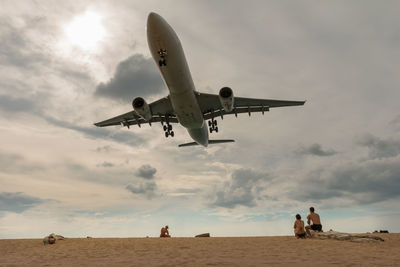 Low angle view of plane flying over beach against sky