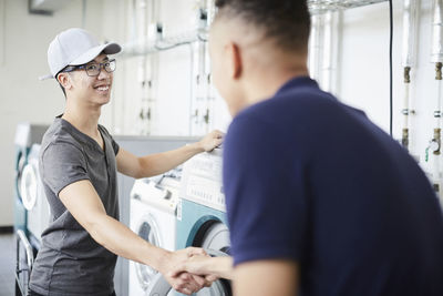 Smiling university friends shaking hands while standing at laundromat