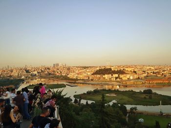 Crowd standing on building terrace looking at cityscape against clear sky