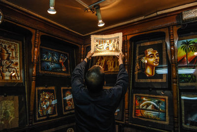Rear view of man holding painting indoors