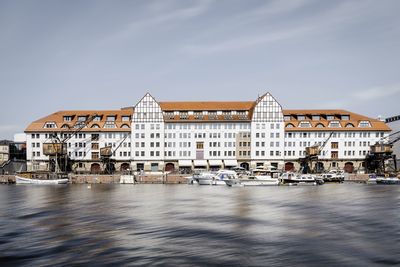 View of buildings by river against cloudy sky