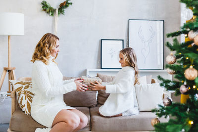 Smiling mother and daughter sitting on sofa at home