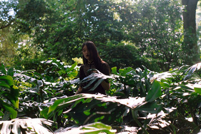 Young woman standing against plants against trees in forest