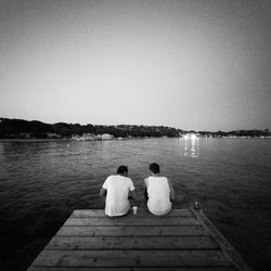 Rear view of couple sitting on lake against clear sky