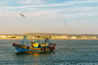 Fishing boats in sea against sky during sunset