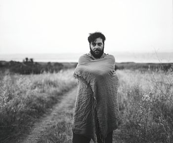 Portrait of mid adult man with scarf standing on grassy field against clear sky