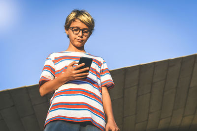 Low angle view of man using smart phone against clear sky